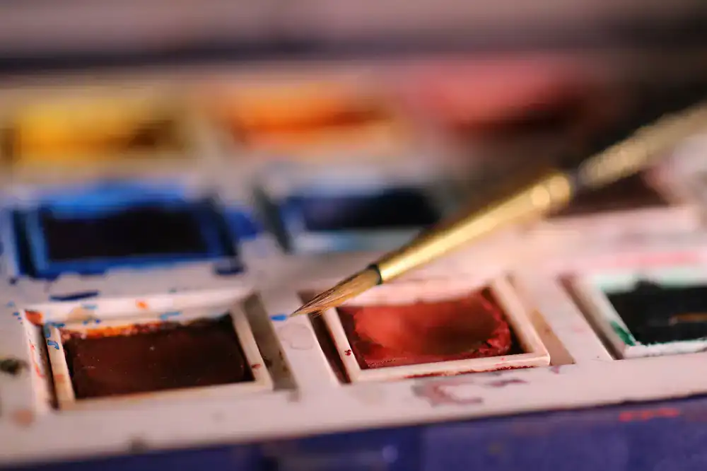 Close up photograph of fine drafting brushes resting beside small ceramic pots of blue pigment